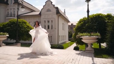 Uzun, havadar peçeli güzel bir gelin, lüks bir saray bahçesinde düğün günü havada uçuşan kumaşla dönen zarif beyaz bir elbise. Çekici, çekici bir kadın kameraya poz veriyor, muhteşem bir elbise içinde..