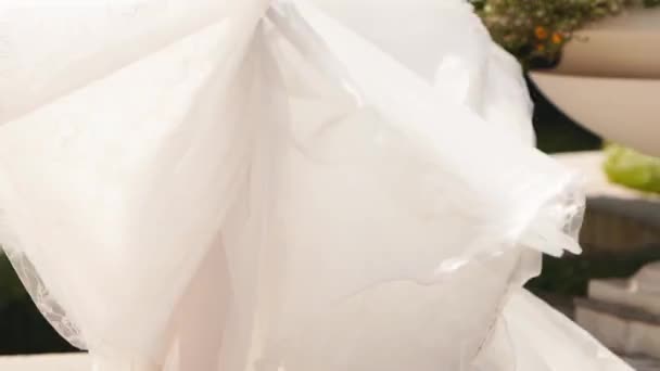 漂亮的新娘戴着长长的飘逸的面纱 优雅的白色婚纱与面料飘扬在一个奢华的宫廷花园的婚礼当天 穿着华丽长袍在镜头前摆姿势的漂亮女人 — 图库视频影像