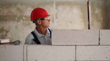 Tuğla ustası lastik çekiç kullanarak beton blokları yıkıyor. Müteahhit, tuğla işi için kesin ruh balonu ve lazer seviyesi kullanır. İşçi yeni apartman dairesine duvar örüyor..