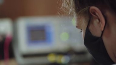 Woman in a protective mask is analyzing electrical signals on an oscilloscope. Laboratory diagnostics of electronic equipment.
