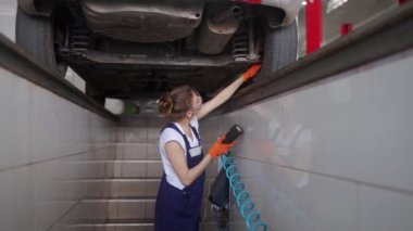Kadın tamirci uzaktan kumandalı hidrolik tekerlek oyun dedektöründe araba süspansiyonunu inceliyor. Tulum giymiş güçlü bir kadın koşu takımlarında yıpranmak ve direksiyon başında direksiyon başına geçmek istiyor.