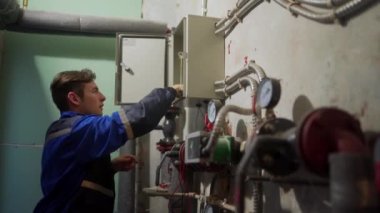 Elektrikçi, sigorta kutusunu inceliyor. Elektriği tamir etmek için elektrik panelini vidalayan üniformalı bir usta. Bölgedeki ısıtma merkezinin teknik odasında kontrol paneli var..