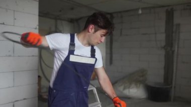 Elektrikçi kabloları döşeyip, eve elektrik kabloları yerleştiriyor. Tulum ve eldiven giyen inşaatçı inşaat alanına elektrik kabloları yerleştiriyor. Adam apartman tadilatı yapıyor..