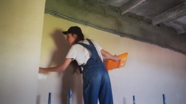 Profesyonel ressam kadın, inşaat alanındaki iskelede paten kayarak duvarı boyuyor. Tulumlu genç bir kadın ev dekorasyonu yapıyor, sahne dekorasyonu yapıyor. İşçi odada DIY onarımı yapıyor.