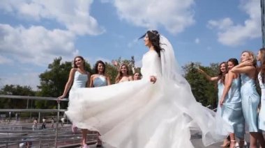 Uzun havadar peçeli güzel bir gelin düğün günü nedimelerle havada uçuşan kumaşla dönen beyaz bir elbise. Çekici bir kadın kameraya poz veriyor ve aynı elbiselerle kız arkadaşları var..