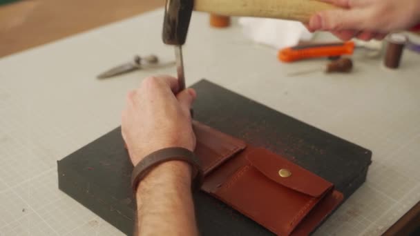 革職人は彼の工房で働いている 革の財布を作るマスター 男カット穴で革パンチングツールステッチパンチとハンマー — ストック動画