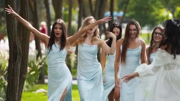 美丽的新娘和漂亮的伴娘穿着浅蓝色的衣服在公园里走着 挥手欢呼 穿着雅致的白色婚纱 头戴长袖婚纱的女人与朋友们聚会 慢动作 — 图库视频影像