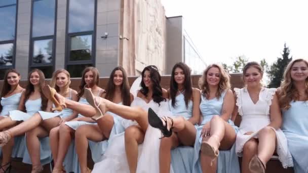 迷人的新娘和伴娘们以挑逗的方式把双腿交叉地坐在长椅上 穿着同一件衣服的漂亮女人在镜头前同时交叉双腿调情 — 图库视频影像