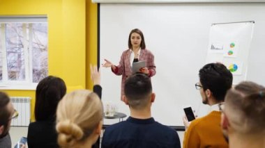 İş kadını antrenörü sunar konferans salonundaki çizelgelerde şemaları gösterir. Proje yöneticisi ofisteki çalışanlara sunum yapacak. Kadın öğretmen ana sınıfı yönetiyor..