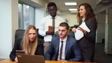 Diverse office corporate workers discuss project on laptop display in office. Multiethnic people planning startup strategy on meeting. Business team consulting on product design on a creative brief.