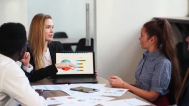 Business woman makes a presentation with charts, diagrams for multiethnic partners. Startup team discuss project plan. Diverse multinational people have meeting in office listening to a supervisor.