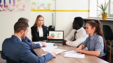 Business woman makes a presentation with charts, diagrams for multiethnic partners. Startup team discuss project plan. Diverse multinational people have meeting in office listening to a supervisor.