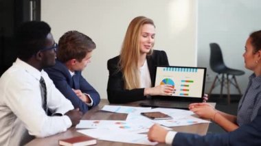 Business woman makes a presentation with charts, diagrams for multiethnic partners. Startup team discuss project plan. Diverse multinational people have meeting in office listening to a supervisor.