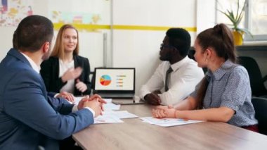 International business partners discuss financial project results on meeting in office. Multiethnic corporate team plans marketing strategy with diagrams, charts, papers, devices. People brainstorming