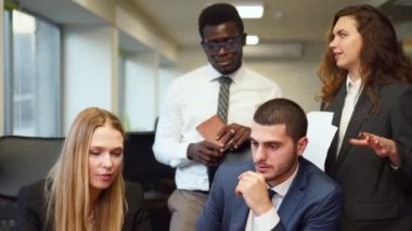 Diverse office corporate workers discuss project on laptop display in office. Multiethnic people planning startup strategy on meeting. Business team consulting on product design on a creative brief.