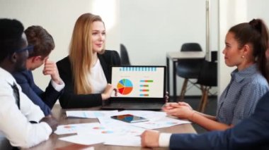 Business woman makes a presentation with charts, diagrams for multiethnic partners. Startup team discuss project plan. Diverse multinational people have meeting in office listening to a supervisor.