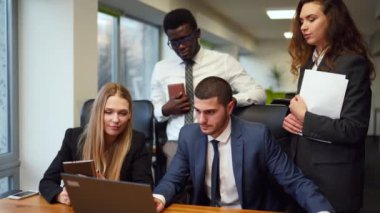 Diverse office corporate workers discuss project on laptop display in office. Multiethnic people planning startup strategy on meeting. Business team consulting on product design on a creative brief.