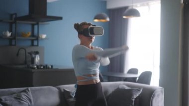 Futuristic girl funny dancing in VR headset for social media platform media in living room at home. Woman avatar performing in metaverse cyberspace immersive experience for her followers audience.