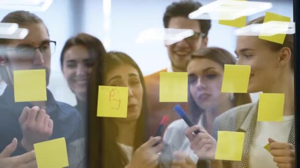 商业团队集思广益 在纸上贴上便条 贴在玻璃墙上 创业同事在公司总部召开的员工代表大会上讨论产品开发工作计划的策略 — 图库视频影像