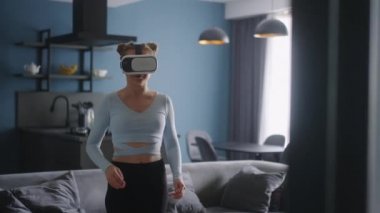 Futuristic girl funny dancing in VR headset for social media platform media in living room at home. Woman avatar performing in metaverse cyberspace immersive experience for her followers audience.
