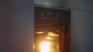 Caucasian woman opens door of heated oven and puts inside pot for baking turns on oven. Young female adult places pan into oven then closes it. Girl fits saucepan inside oven closeup shot.
