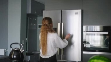 Young woman taking orange from fridge throwing it up. Girl getting fruit from refrigerator. Female having something healthy for snack. Caucasian woman is about to cut orange. Girl cutting orange