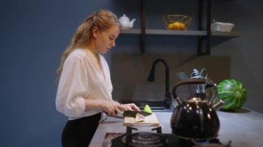 Young woman cuts fruit and takes chocolate pie out of the oven. Girl makes, smells and shows dessert. Female performs homemade baking in modern kitchen. Housewife prepares pastry on kitchen island