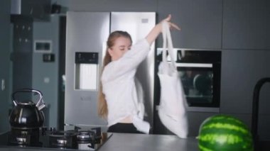 Economical inflation. Woman in kitchen looking at cash receipt and counting after shopping. Girl checks bill and calculates expenses at home after buying groceries. Female looking at phone.