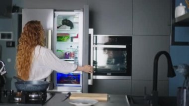 Young woman taking tomatos from fridge to cut them on chopping board. Girl getting tomato from refrigerator. Female having something healthy for snack. Caucasian woman is about to eat ameal.