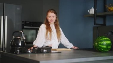 Portrait of blonde caucasian woman crossing arms and smiling in kitchen. Young cheerful adult female folding hands standing at home in modern interior