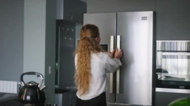 Young woman taking orange and apple from fridge. Girl getting fruit from refrigerator. Female having something healthy for snack. Caucasian woman is about to cut orange. Girl cutting orange