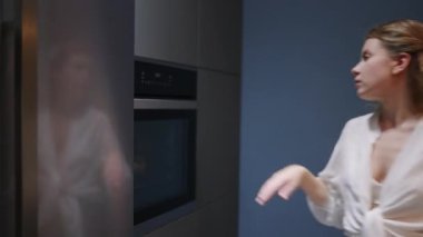 Young woman takes chocolate pie out of the oven. Girl makes pastry at home. Female performs homemade baking in a stylish modern kitchen. Housewife prepares and smells dessert, smiles on camera closeup