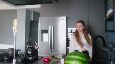 Food blogger woman cooking fresh vegan salad of vegetables in kitchen studio and filming funny dancing for social media content on a smartphone for a video channel. Female influencer streaming.