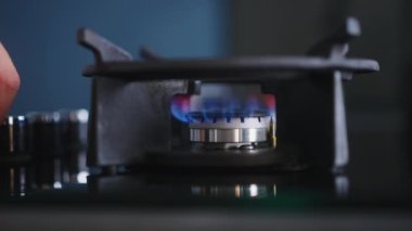 Human hand turns on kitchen cooktop gas burner and natural gas ignites burns with a blue flame. Person hand lighting gas stove burner closeup shot. Household faces rise in gas prices