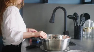 Young caucasian woman washes pots under running water in sink in modern kitchen. Housewife is rinsing the pan on a kitchen island. Female performing the washing-up in high-tech kitchen