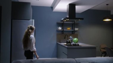 Young woman takes chocolate pie out of the oven. Girl makes pastry at home. Female performs homemade baking in stylish modern kitchen. Housewife prepares and smells food on kitchen island, takes knife