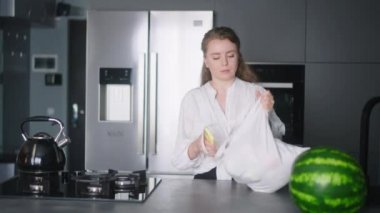 Economical inflation. Woman in kitchen looking at cash receipt and counting after shopping. Girl checks bill and calculates expenses at home after buying groceries. Female looking at phone.