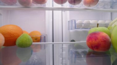 View from inside the fridge - woman opens side by side fridge doors, puts tomatos, then closes it. Female puts vegetables into refrigerator. Pretty girl on healthy diet.