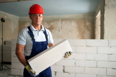 Tuğlacı ya da duvarcı otoklastlı beton bloklardan duvar inşa ediyor. Kaliteli köpüklü betonla inşaat alanında inşaat yapan tuğla işçilerinin portresi.