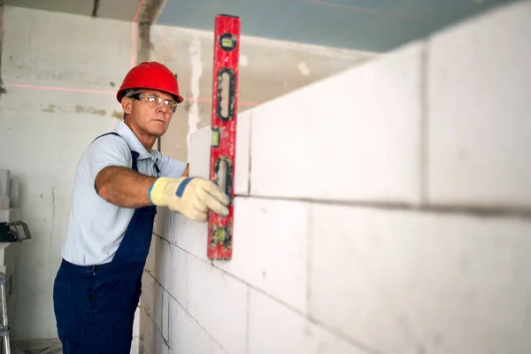 Bricklayer using spirit bubble and laser level to precise check concrete blocks on a wall. Contractor uses tools for brickwork. Worker constructs a wall in new apartment real estate.