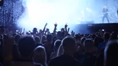 People silhouettes jump waving and clapping hands, crazy dancing with hand-horns at live music concert at open air festival. Fans at a favourite rock band performance.
