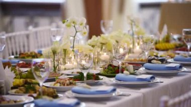 Wedding rustic style decor with dishes, drinks and roses in white and blue colours on table setting at restaurant. Banquet hall interior floristic details, flowers in glass vases filled with water.