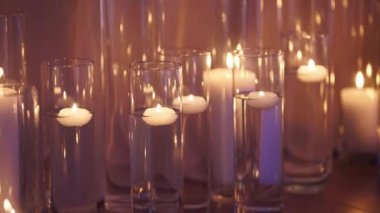Floating candles burning in glass vases filled with water near a white wedding table tablecloth. Boho rustic decor. Birthday party decoration. Sorrow, funeral or mourning candles concept.