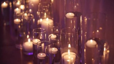 Floating candles burning in glass vases filled with water near a white wedding table tablecloth. Boho rustic decor. Birthday party decoration. Sorrow, funeral or mourning candles concept.