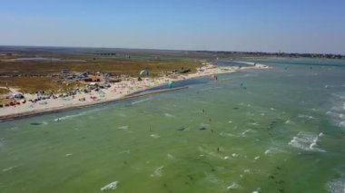 Aerial of many kiteboarders with colorful kites flying over the blue sea lagoon ride on kiteboards. Kitesurfers surf on waves with parachutes on a windy day. Drone video.