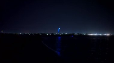 2020-07-25 - Henychensk, Ukraine. Person rides on illuminated kiteboard in the sea with glowing kite at night. Man surfing on a kitesurf with lit parachute on ocean waves in the dark. Extreme sport.