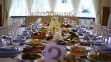 Wedding rustic style decor with dishes, drinks and roses in white and blue colours on table setting at restaurant. Banquet hall interior floristic details, flowers in glass vases filled with water.