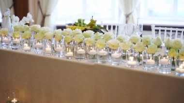 Wedding rustic style decor with dishes, drinks and roses in white and blue colours on table setting at restaurant. Banquet hall interior floristic details, flowers in glass vases filled with water.
