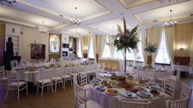 Wedding rustic style decor with dishes, drinks and roses in white and blue colours on table setting at restaurant. Banquet hall interior floristic details, flowers in glass vases filled with water.