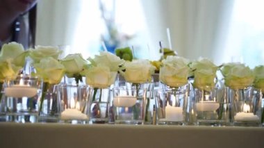 Wedding rustic style decor with dishes, drinks and roses in white and blue colours on table setting at restaurant. Banquet hall interior floristic details, flowers in glass vases filled with water.